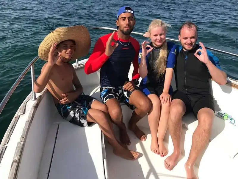 Quatre personnes souriantes sur un bateau en mer, geste OK