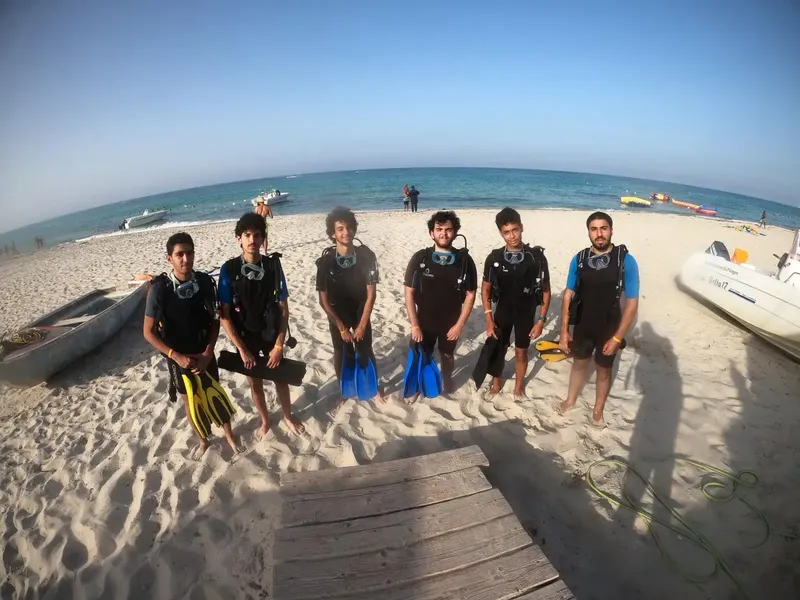 Groupe de plongeurs équipés sur une plage ensoleillée avec bateaux