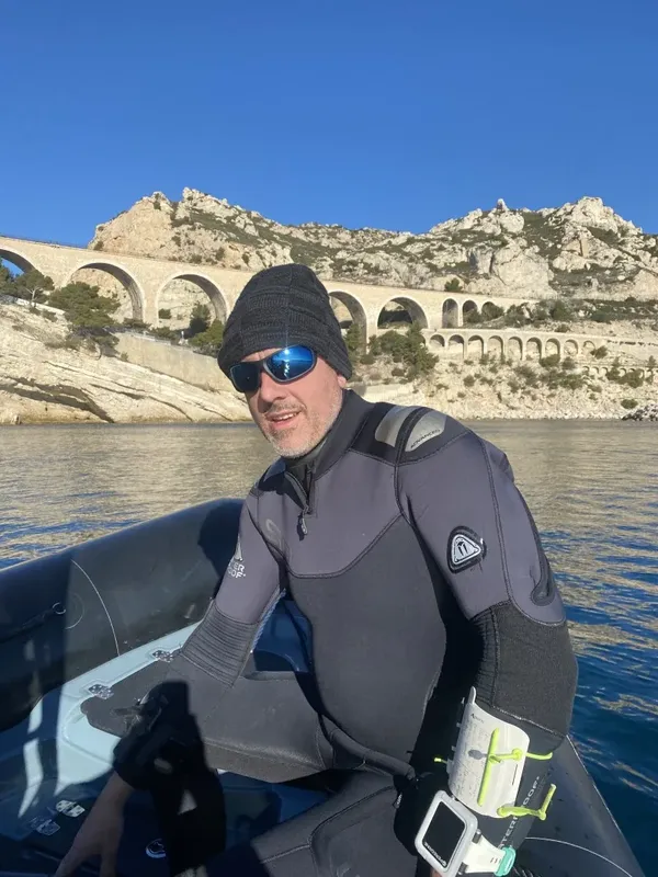 Plongeur en combinaison noire sur un bateau, regardant la caméra