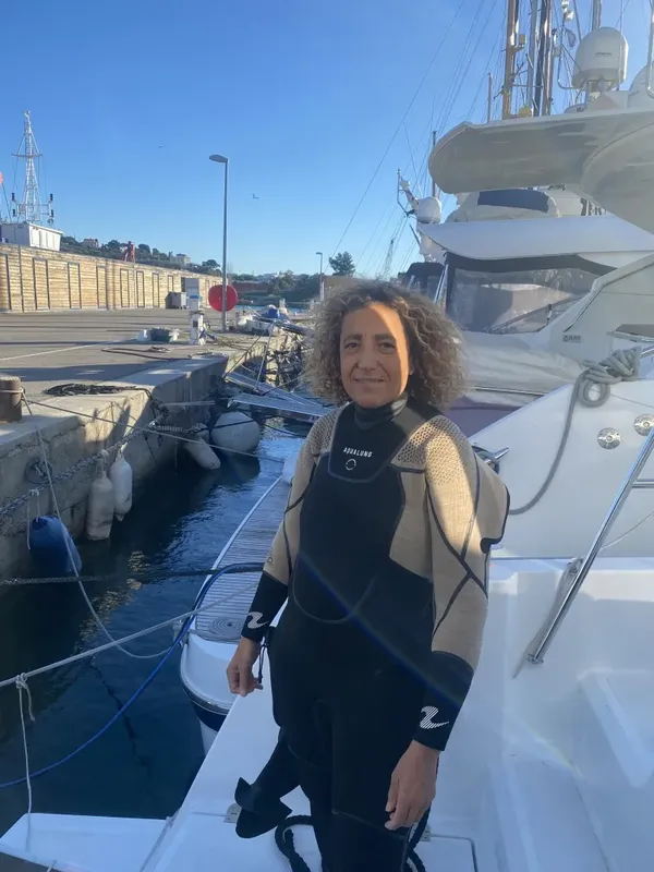 Une plongeuse souriante se tient sur un ponton près des bateaux