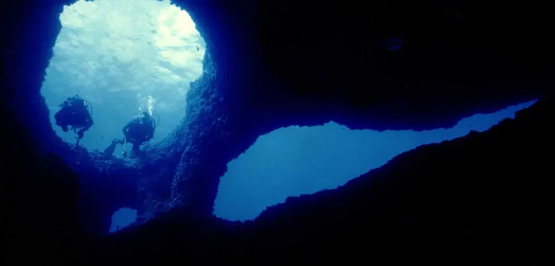Deux plongeurs explorent une grotte sous-marine, lumière filtrant en surface