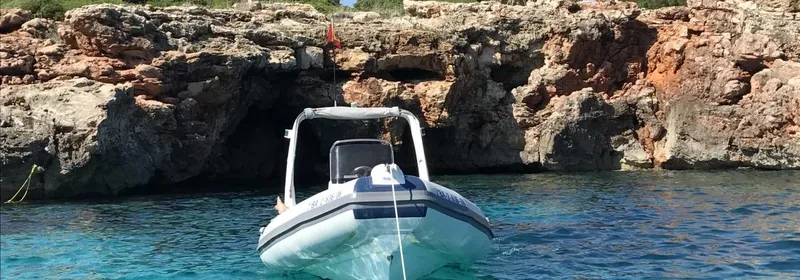 Bateau semi-rigide amarré devant une falaise rocheuse en bord de mer