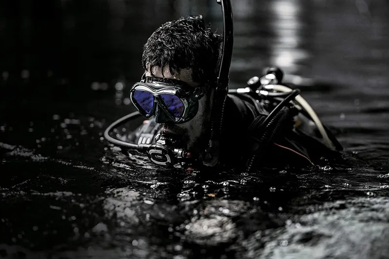 Plongeur avec masque et détendeur nageant dans une eau sombre