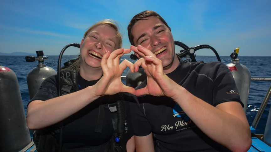 Deux plongeurs souriants forment un cœur avec leurs mains en mer