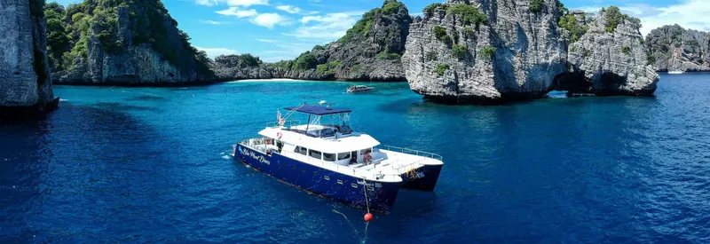 Catamaran bleu navigue dans une baie turquoise entourée de falaises