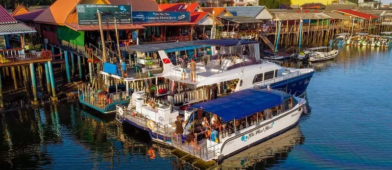 Plusieurs bateaux de plongée amarrés devant des bâtiments colorés et des personnes