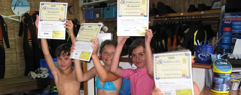 Trois enfants souriants brandissent leurs certificats de formation à la plongée