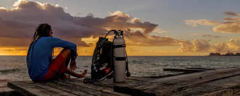 Plongeur assis sur un ponton avec son équipement au coucher du soleil