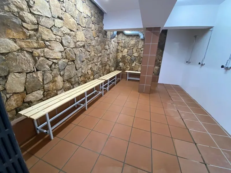 Vestiaire avec bancs en bois, sol carrelé et mur en pierre