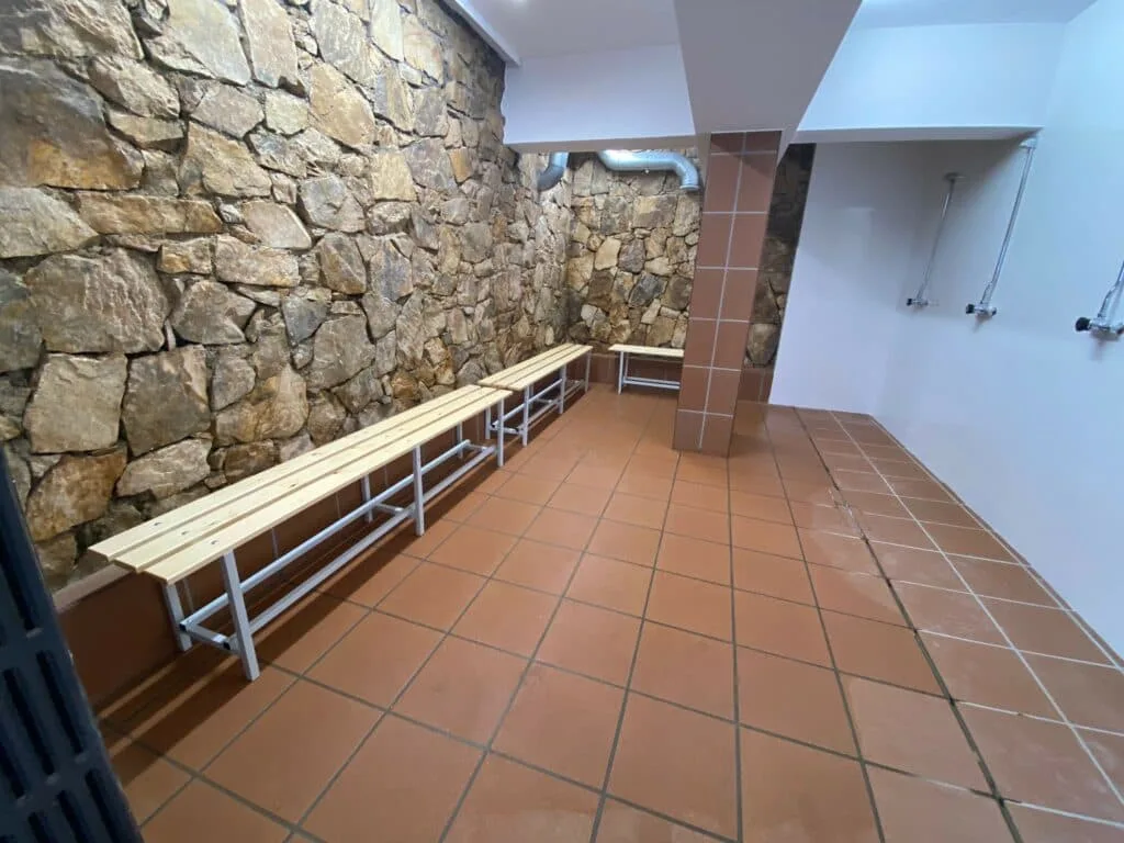 Vestiaire avec bancs en bois, sol carrelé et mur en pierre