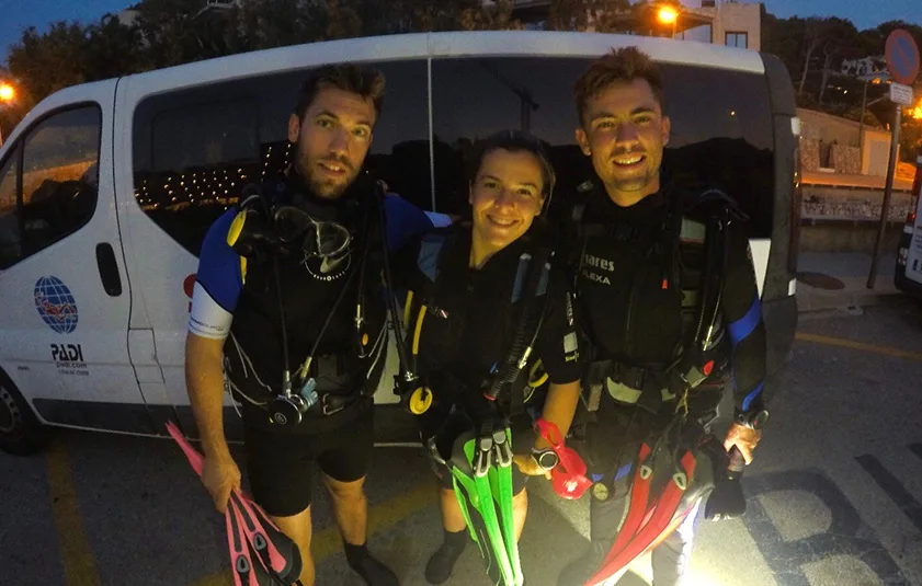 Trois plongeurs souriants équipés devant un véhicule avec logo PADI