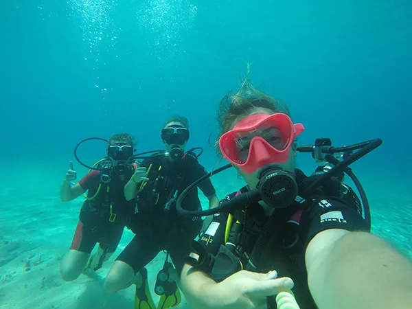 Trois plongeurs souriants prennent un selfie sous l'eau en mer