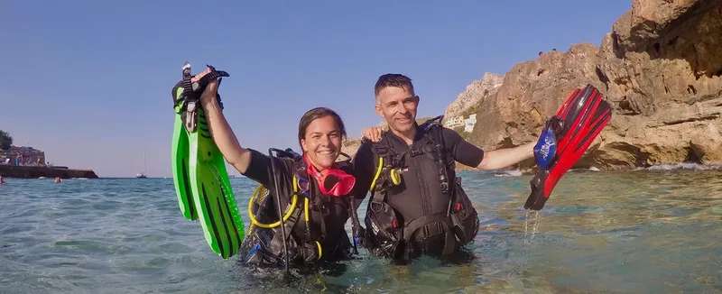 Deux plongeurs souriants sortent de l'eau avec leur matériel