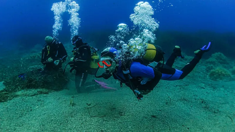 Trois plongeurs explorent les fonds marins, bulles et sable