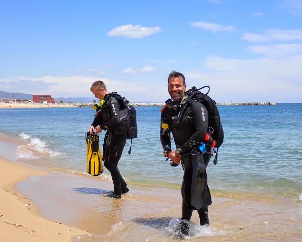 Deux plongeurs équipés sortent de l'eau sur une plage ensoleillée