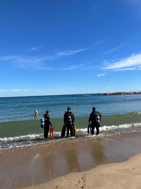 Trois plongeurs équipés se tiennent sur une plage ensoleillée