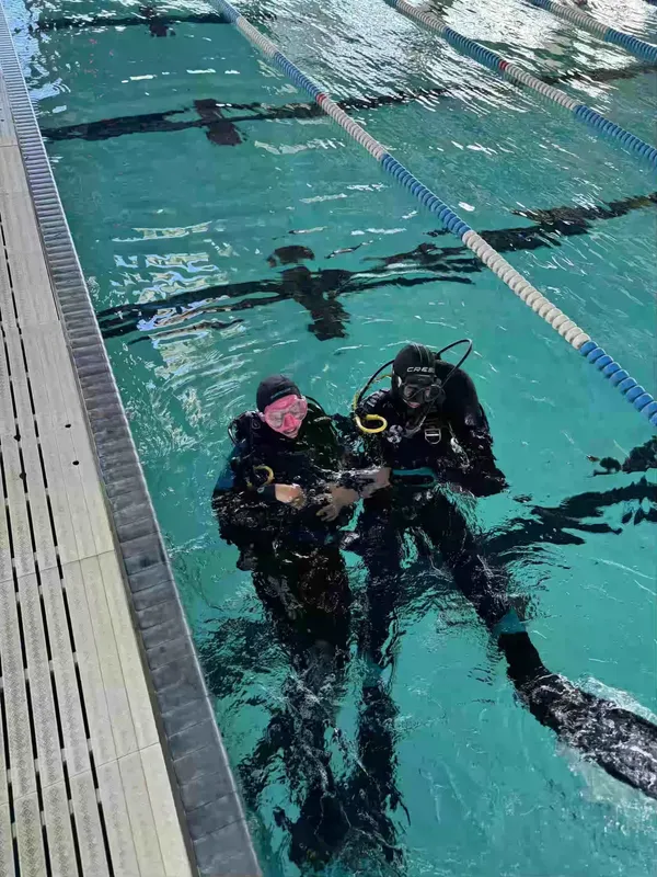 Deux plongeurs en combinaison s'entrainent dans une piscine claire