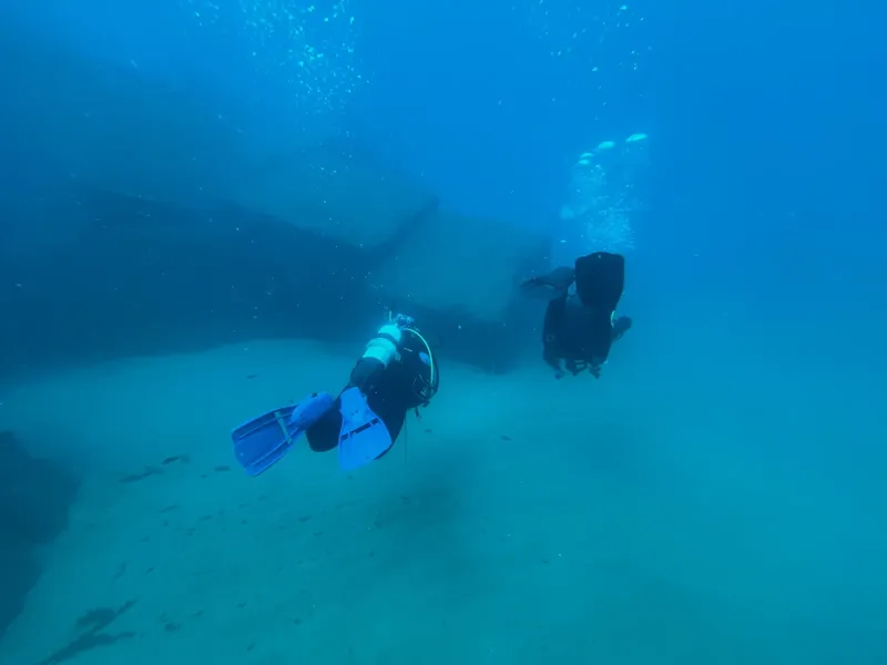 Deux plongeurs explorent une épave sous-marine dans une eau turquoise