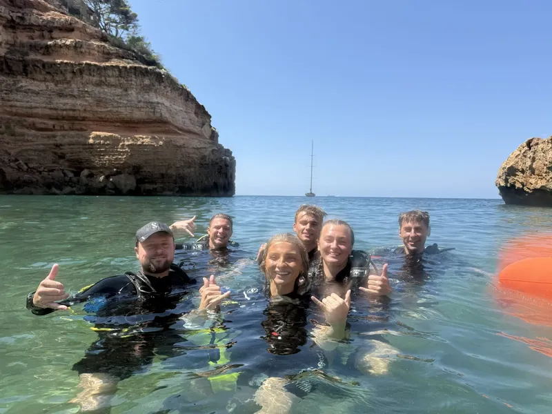 Groupe de plongeurs souriants dans l'eau, côte rocheuse en arrière-plan