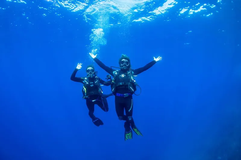Deux plongeurs souriants bras ouverts dans une eau bleue claire