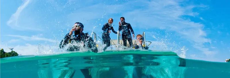 Plongeurs souriants sur un bateau, moitié dans l'eau, ciel bleu