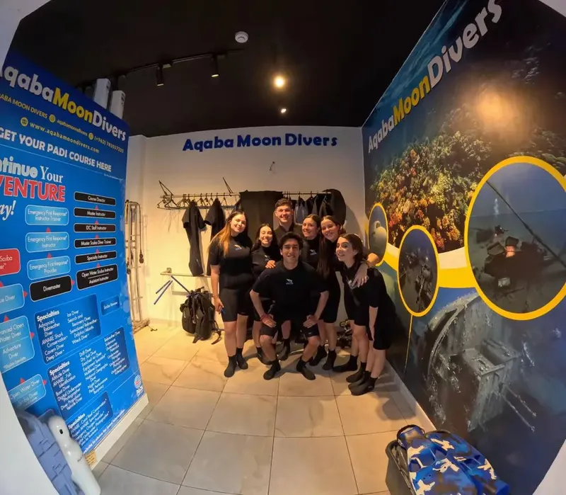 Groupe de plongeurs souriants devant une structure avec des informations PADI