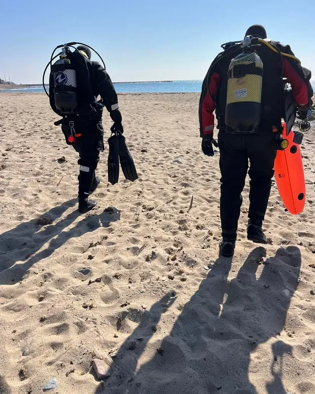 Deux plongeurs marchant sur une plage de sable avec leur équipement