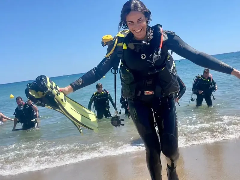 Plongeuse souriante sortant de l'eau avec son équipement complet