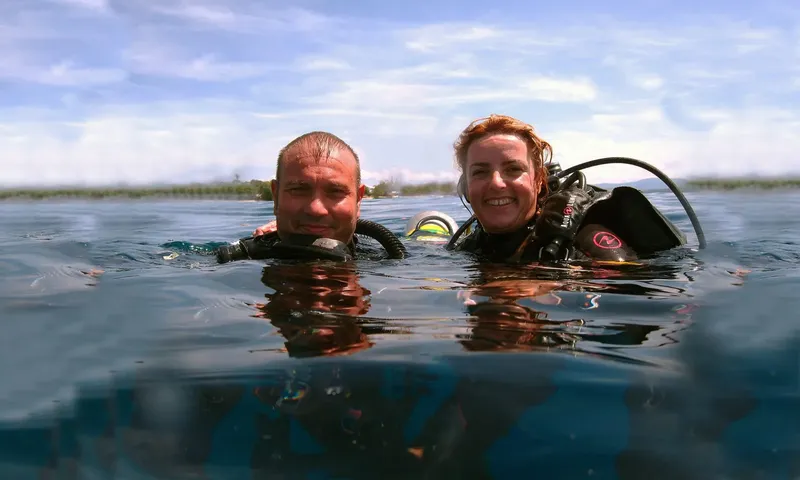 Deux plongeurs souriants émergent à la surface de l'eau bleue
