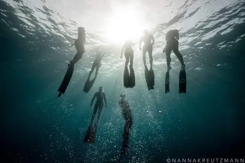 Groupe de personnes en apnée, nageant vers la surface lumineuse