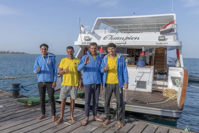 Quatre personnes souriantes posent devant un bateau de plongée amarré