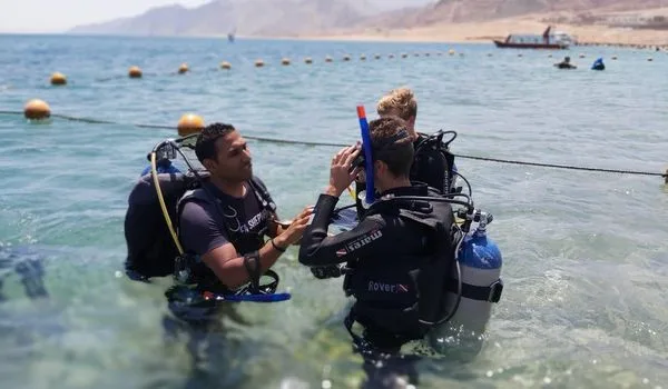Plongeurs préparant l'équipement sur une plage ensoleillée avec un bateau
