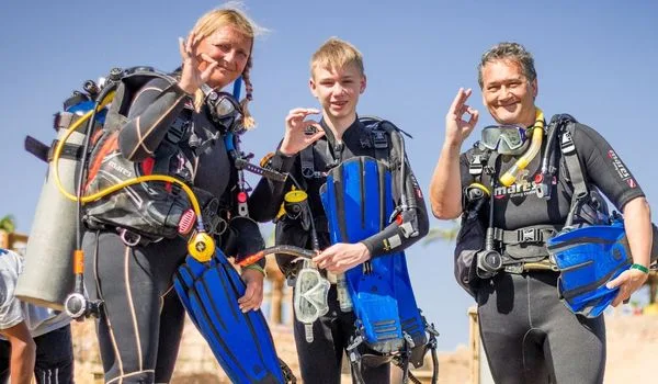 Trois plongeurs équipés sourient à la caméra, prêts pour une immersion