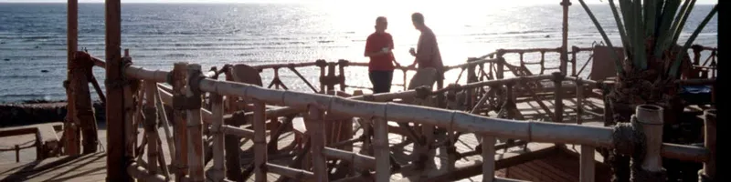 Deux personnes discutent sur une terrasse en bois face à la mer