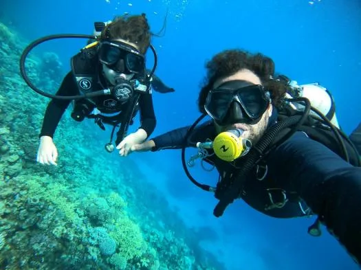 Deux plongeurs souriants explorent un récifal corallien en bleu profond