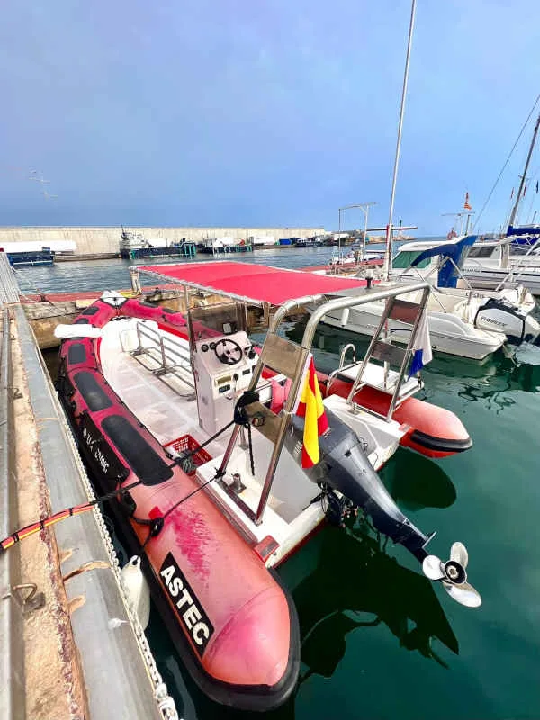 Bateau de plongée rouge amarré dans un port ensoleillé avec des voiliers
