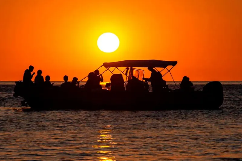 Silhouette de personnes à bord d'un bateau au coucher du soleil