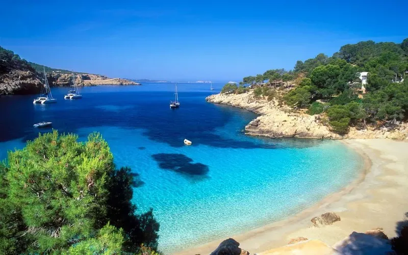 Crique de sable blanc avec des bateaux à voile dans une eau turquoise