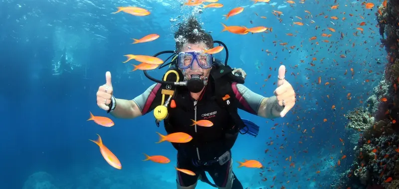 Plongeur souriant avec pouces levés entouré de poissons colorés