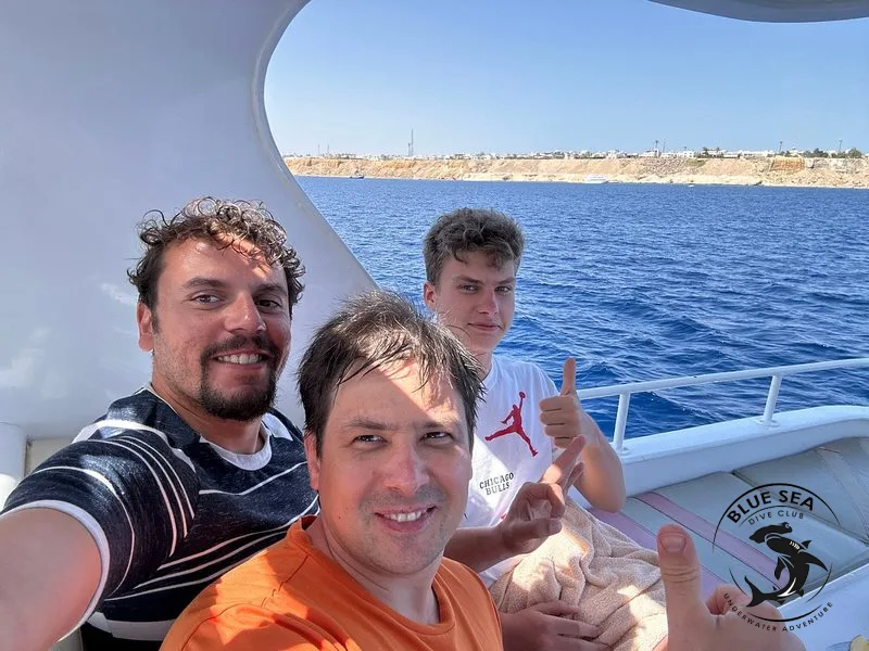 Trois personnes souriantes sur un bateau en mer, ciel bleu