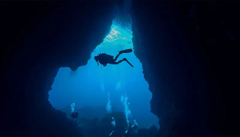 Plongeur explorant une grotte sous-marine avec des rayons de lumière