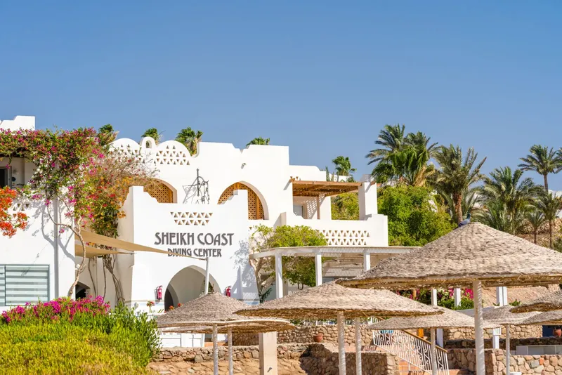 Bâtiment blanc avec enseigne, parasols de plage et végétation tropicale