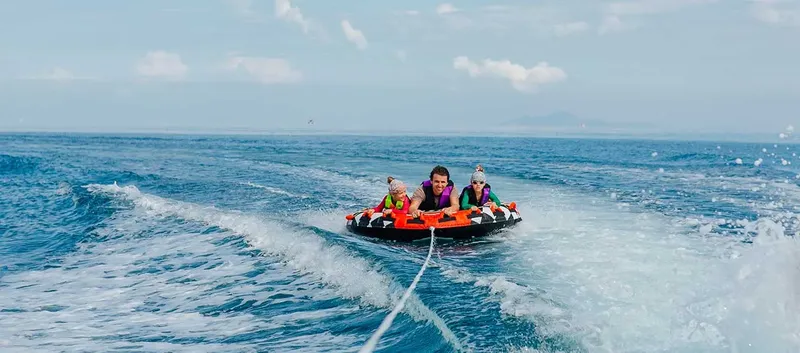 Trois personnes sourient, tractées sur une bouée gonflable en mer