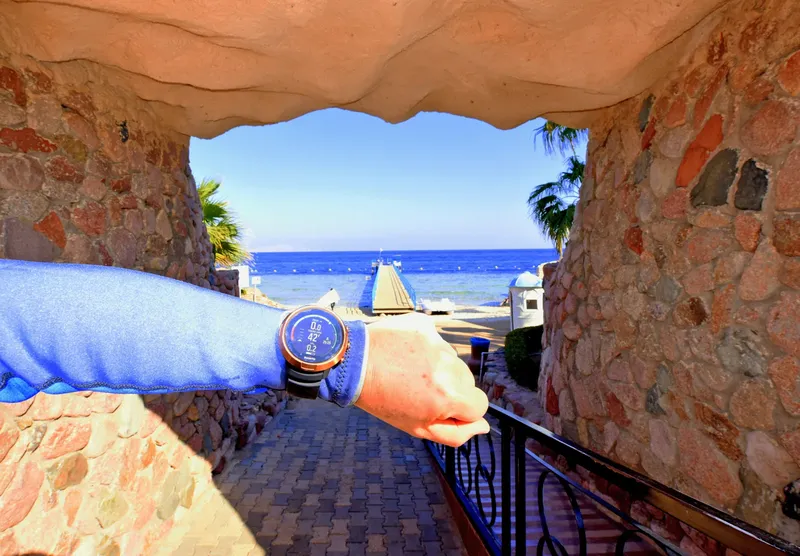 Bras tendu avec une montre de plongée, vue sur la mer et plage