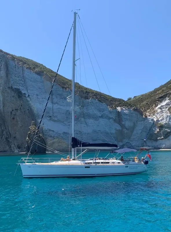 Voilier amarré dans une crique turquoise, avec des personnes à bord