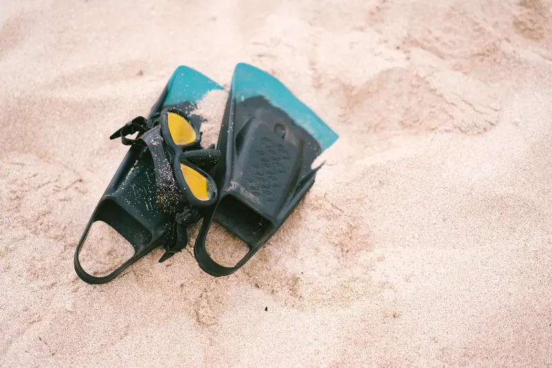 Paire de palmes de plongée noires et turquoise sur sable clair