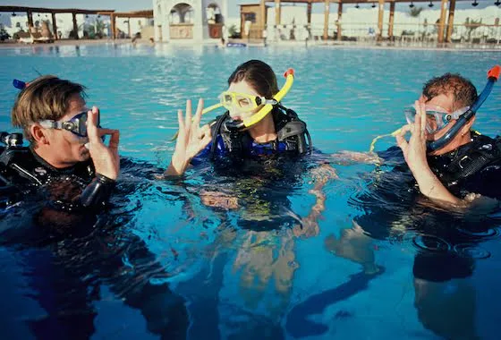 Trois plongeurs en formation, équipés, dans une piscine bleu clair