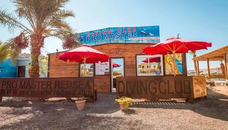 Façade d'un club de plongée avec parasols rouges et palmiers
