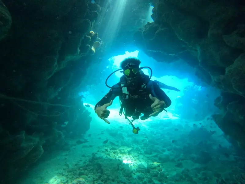 Plongeur en combinaison explore une grotte sous-marine éclairée par le soleil