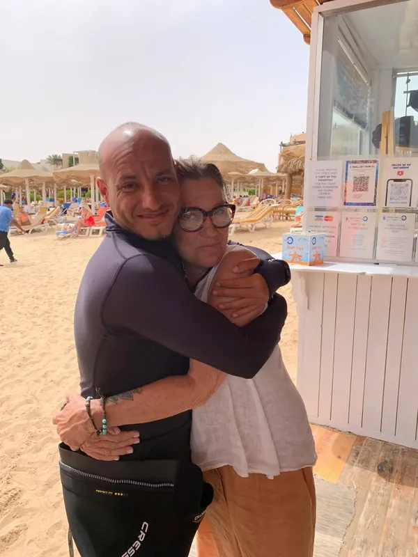 Deux personnes s'embrassent sur une plage devant un petit bâtiment